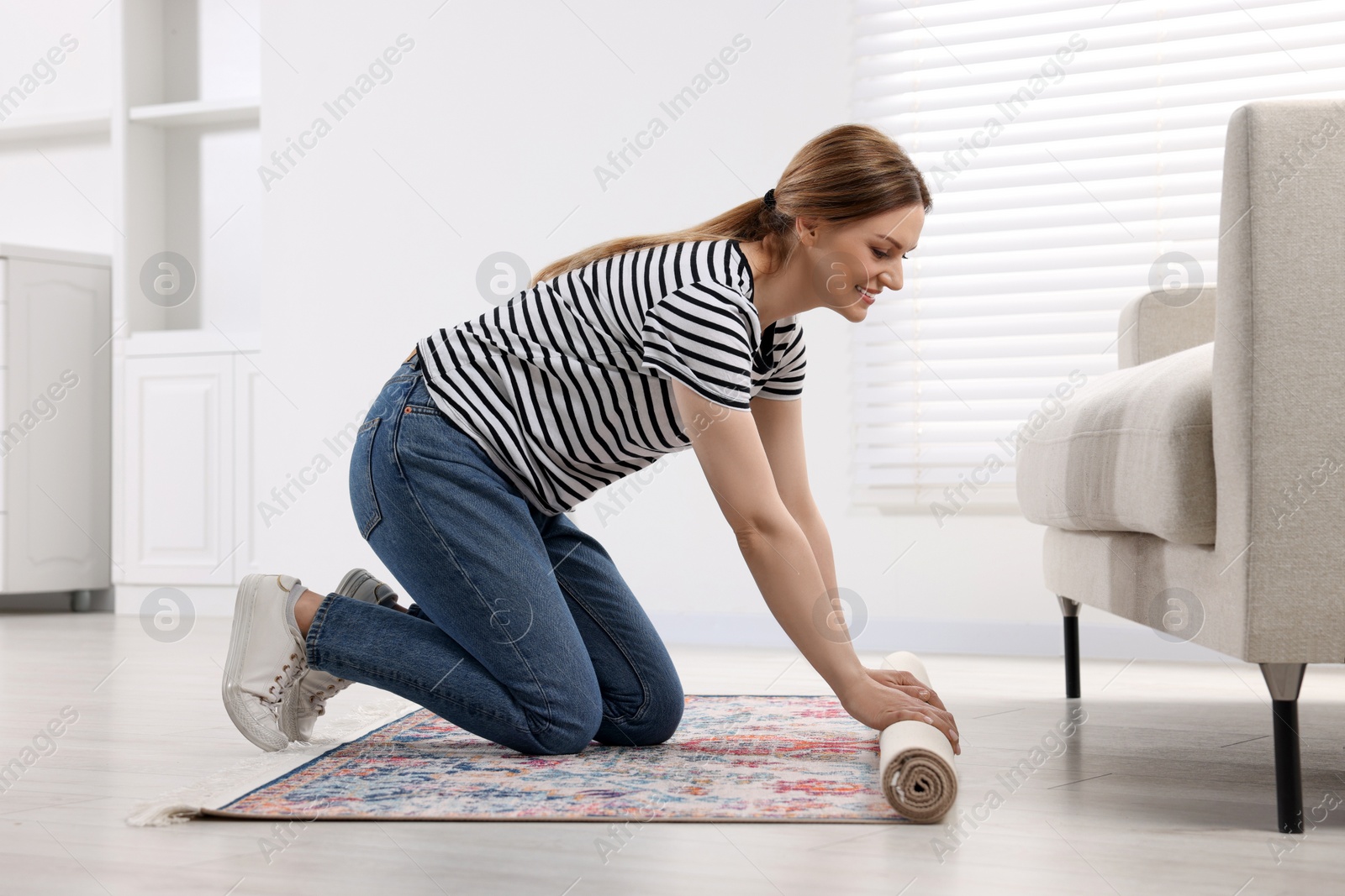 Photo of Smiling woman unrolling carpet with beautiful pattern on floor in room