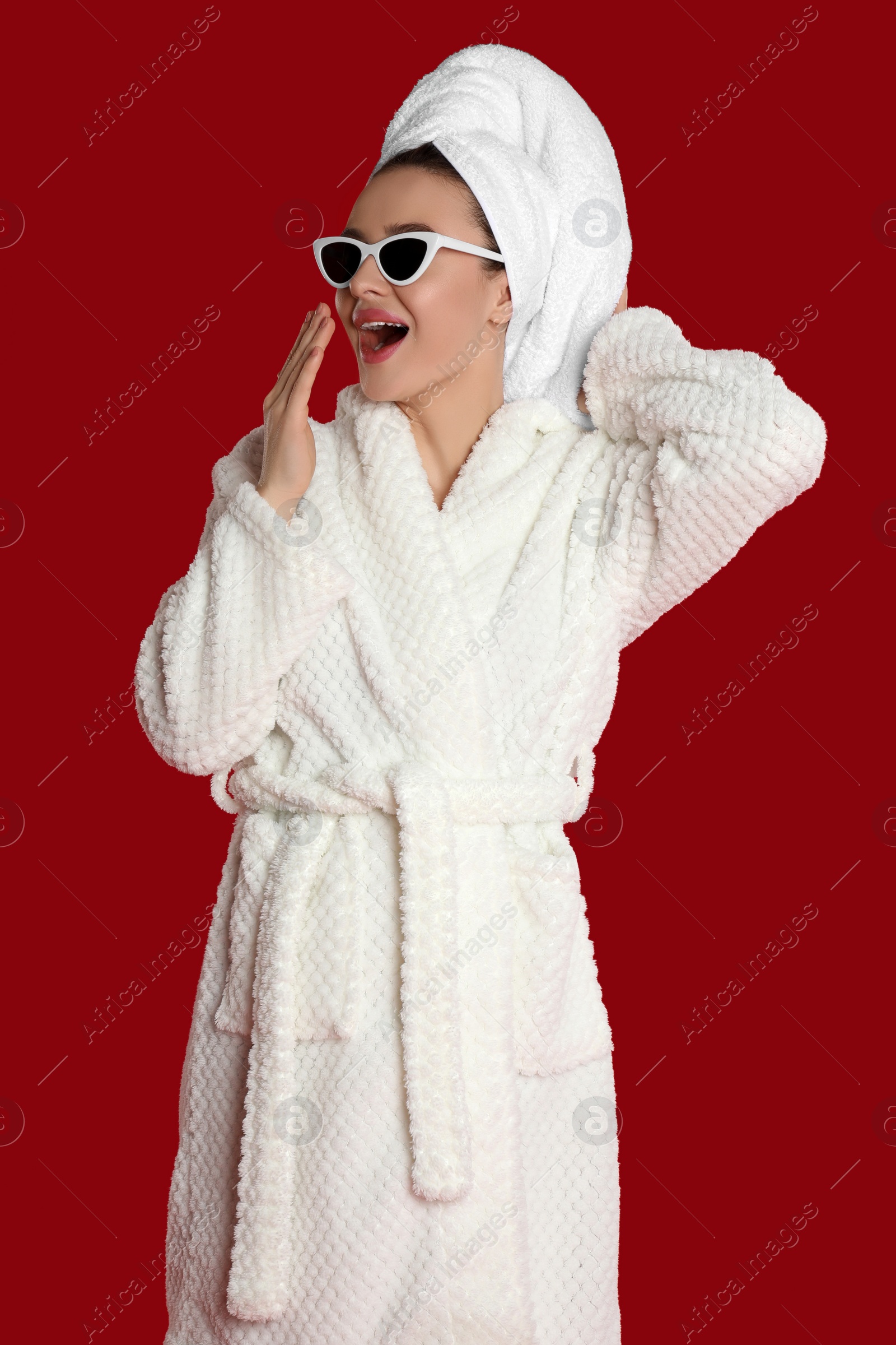 Photo of Beautiful young woman in bathrobe and sunglasses yawning on red background