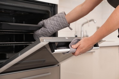 Woman putting baking tray into electric oven in kitchen, closeup