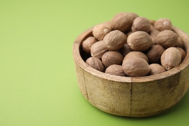 Whole nutmegs in bowl on light green background, closeup. Space for text