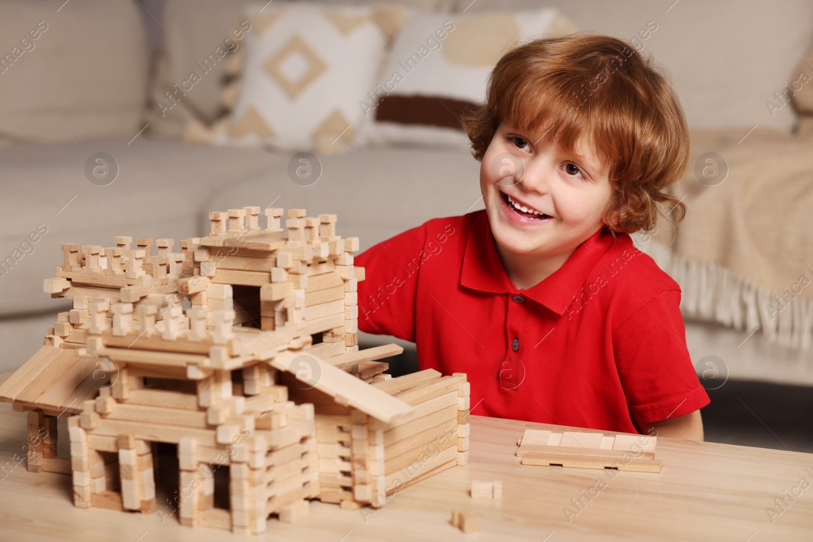 Photo of Cute little boy playing with wooden castle at table in room. Child's toy