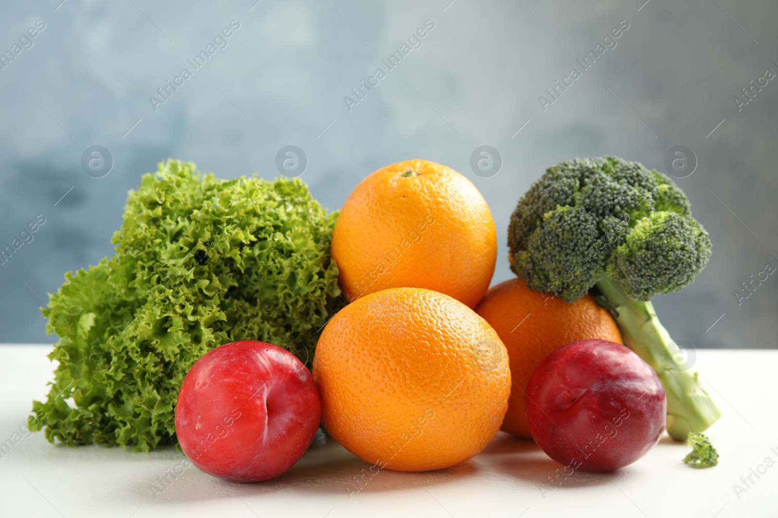 Photo of Fresh fruits and vegetables on white table against light blue background