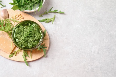 Photo of Bowl of tasty arugula pesto and ingredients on light table, flat lay. Space for text