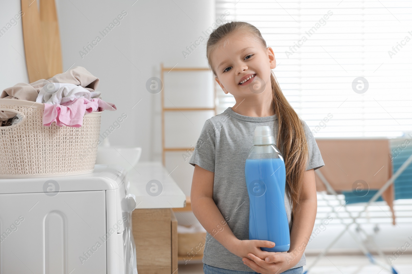 Photo of Little girl holding fabric softener in bathroom, space for text