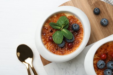 Delicious creme brulee with berries and mint in bowls on white wooden table, top view