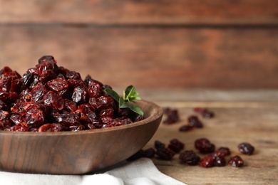 Photo of Dried cranberries in bowl on wooden table, closeup. Space for text