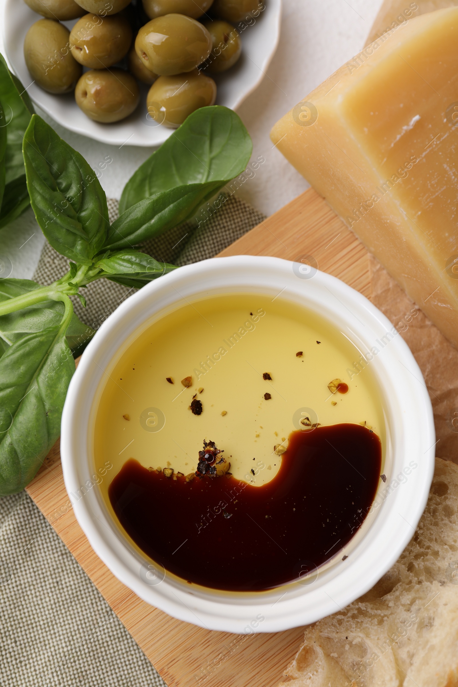 Photo of Bowl of organic balsamic vinegar with oil, basil, bread, cheese and olives on table, flat lay