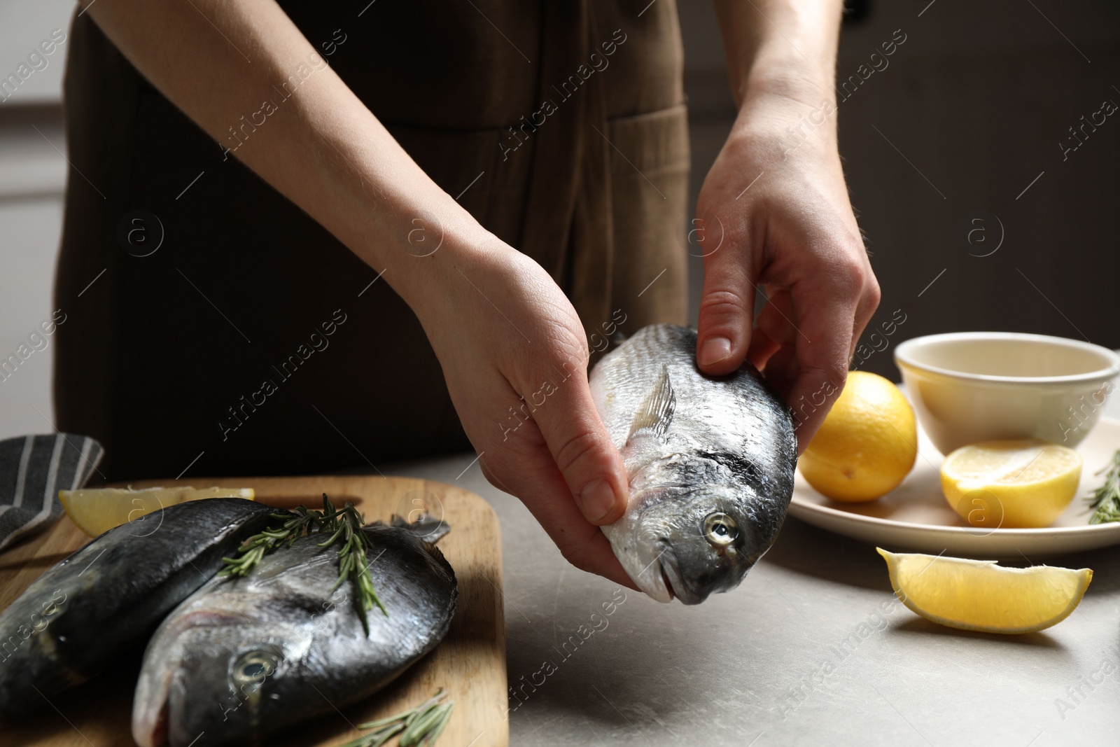 Photo of Woman holding dorada fish over grey table, closeup