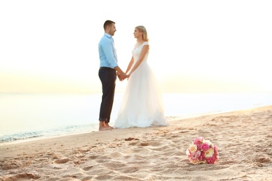 Bouquet and wedding couple on beach. Space for text