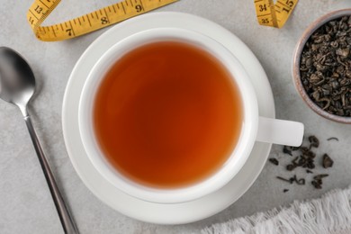 Cup of herbal diet tea and measuring tape on white table, flat lay. Weight loss concept