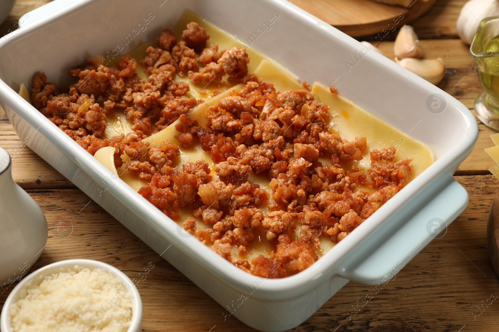 Photo of Cooking lasagna. Pasta sheets and minced meat in baking tray on wooden table, closeup