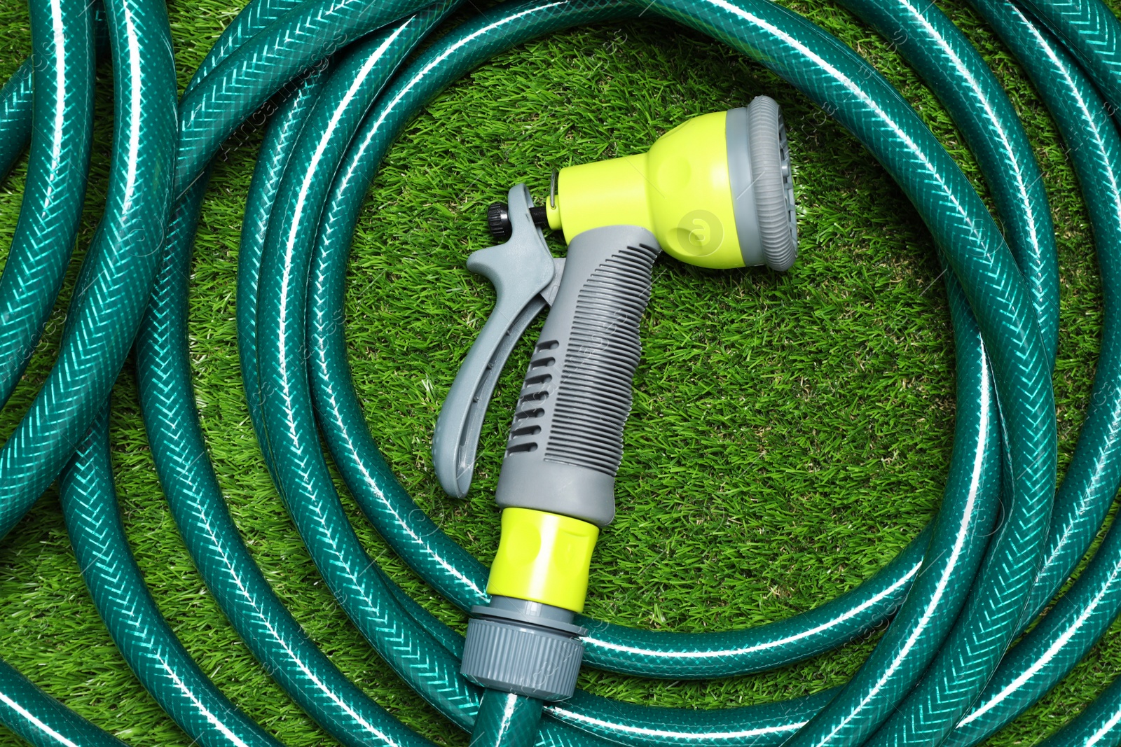 Photo of Watering hose with sprinkler on green grass, top view