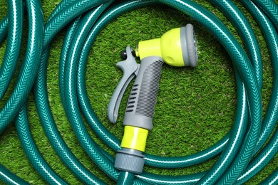 Photo of Watering hose with sprinkler on green grass, top view