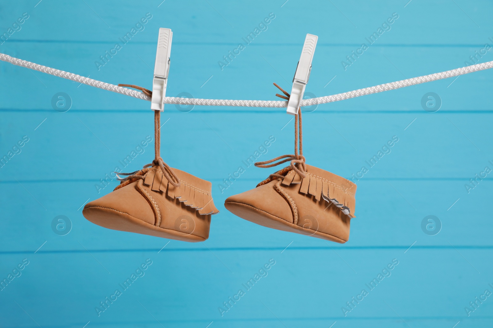 Photo of Cute baby shoes drying on washing line against light blue wooden wall