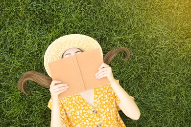 Photo of Young woman reading book on green grass, top view