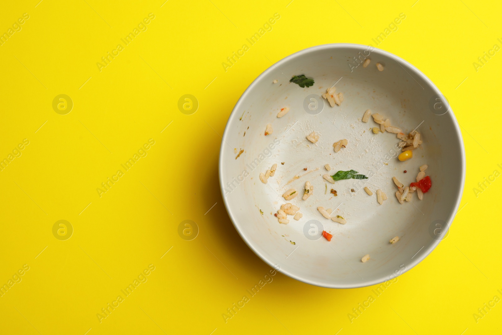 Photo of Dirty bowl with food leftovers on yellow background, top view. Space for text