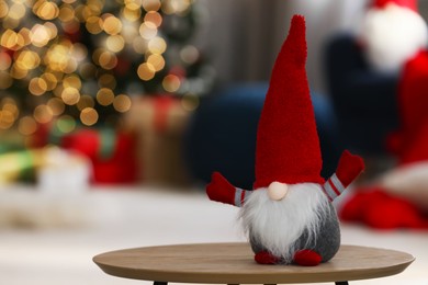 Photo of Cute Christmas gnome on wooden table in decorated room, space for text