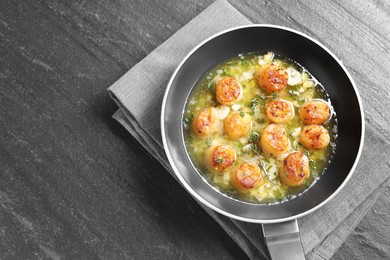 Delicious scallops with sauce in frying pan on dark gray textured table, top view. Space for text