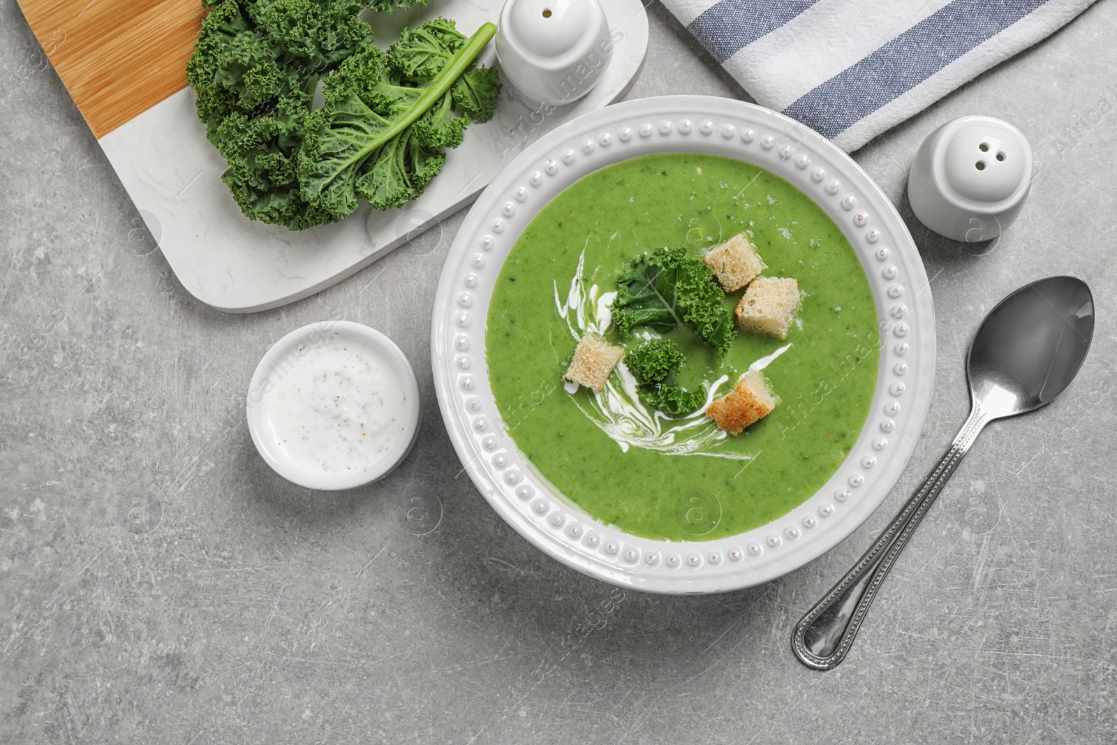 Photo of Tasty kale soup with croutons served on grey table, flat lay