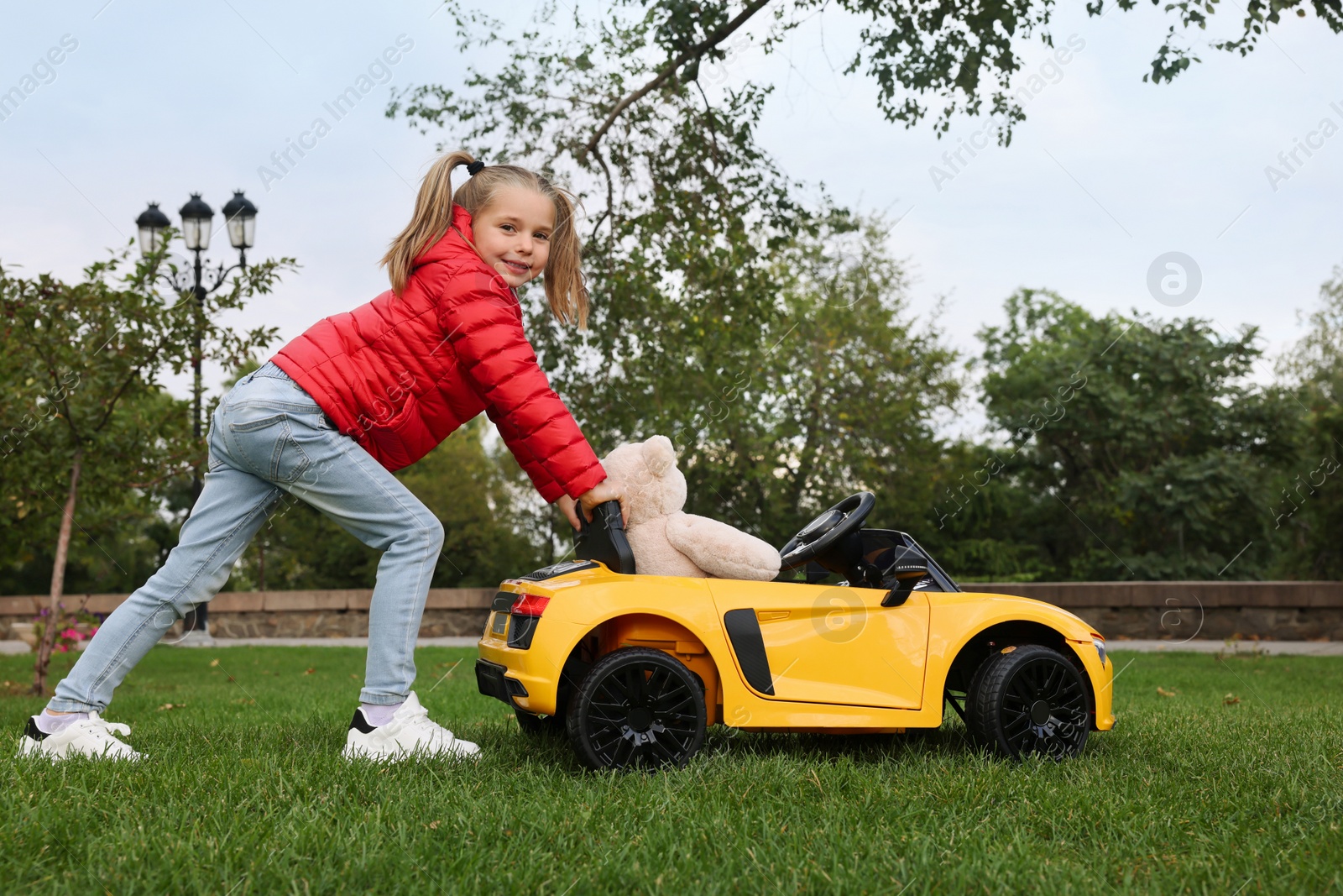 Photo of Cute little girl playing with toy bear and children's car in park