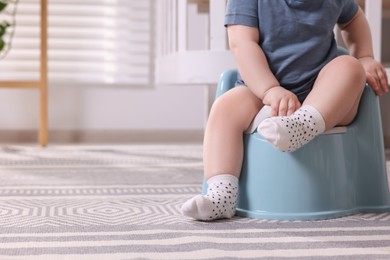 Photo of Little child sitting on plastic baby potty indoors, closeup. Space for text