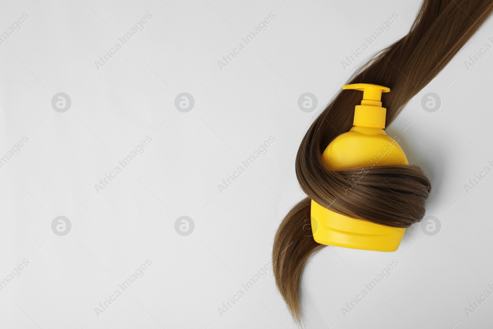 Photo of Shampoo bottle wrapped in lock of hair isolated on white, top view. Natural cosmetic products