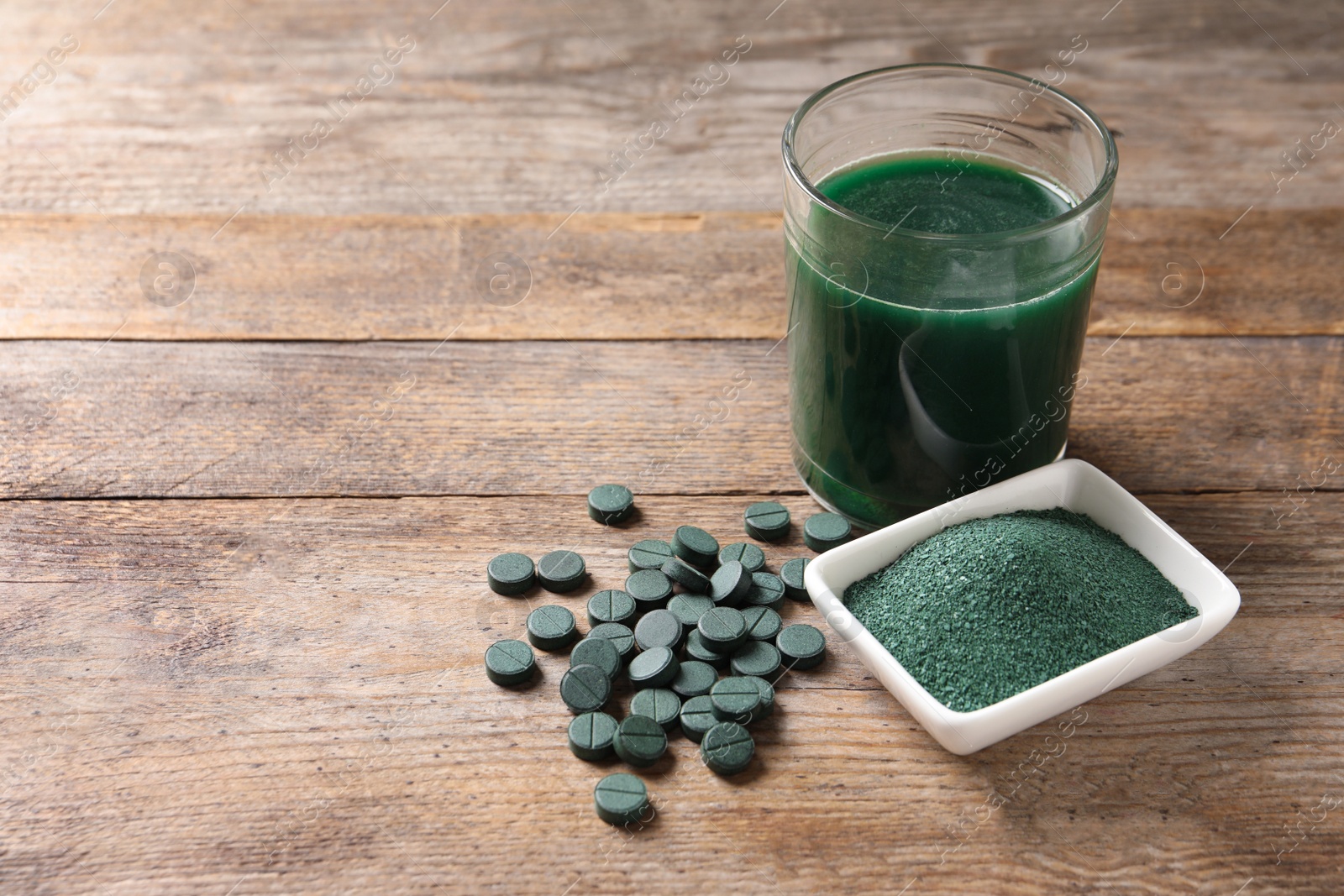 Photo of Spirulina powder, pills and drink on wooden background, space for text