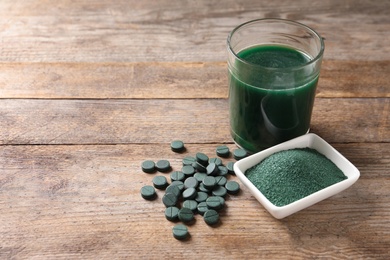 Spirulina powder, pills and drink on wooden background, space for text