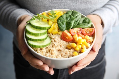 Photo of Woman holding bowl with healthy quinoa salad and vegetables, closeup