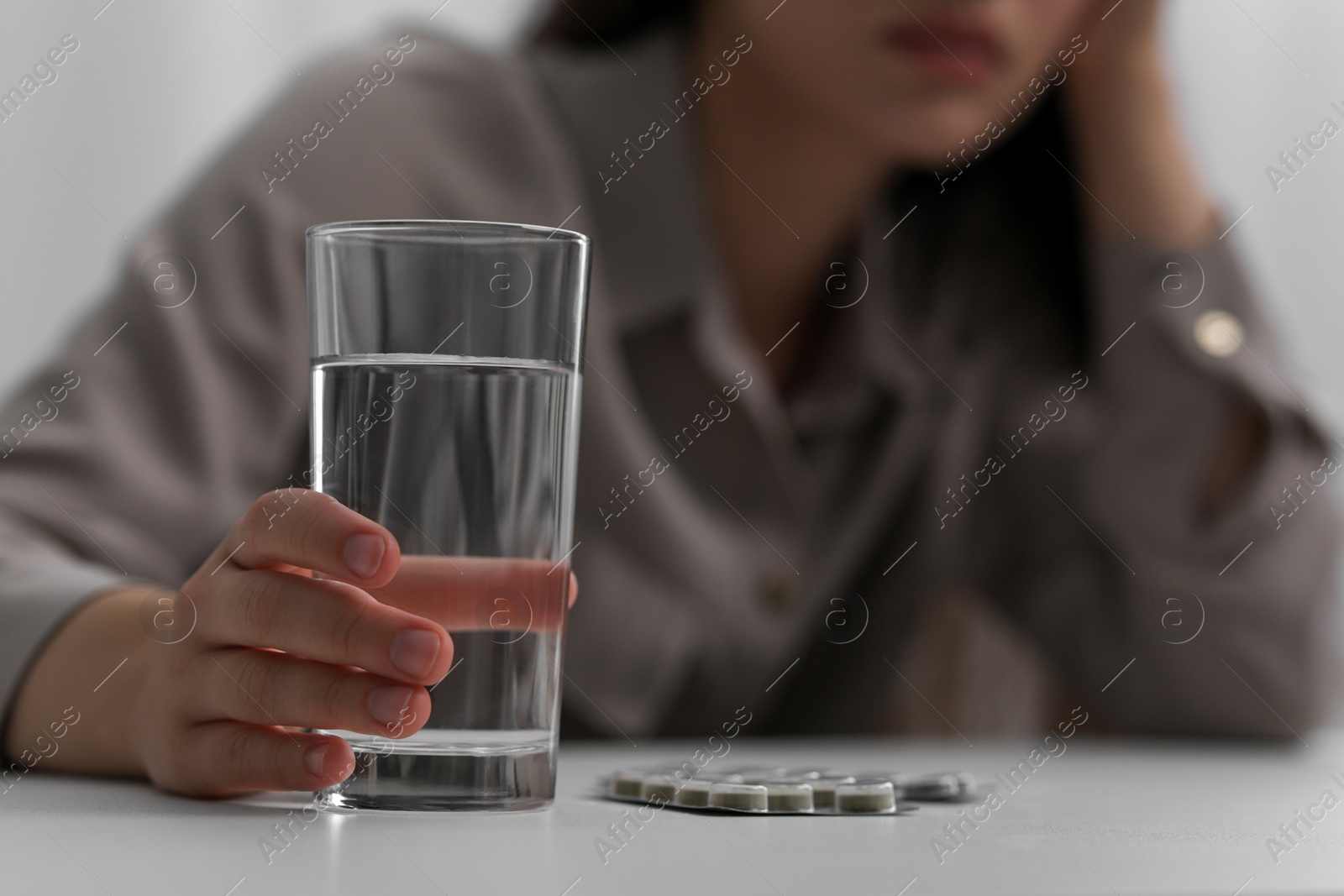 Photo of Woman with glass of water and antidepressant pills at white table, closeup. Space for text