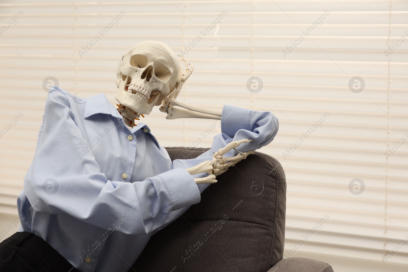 Photo of Waiting concept. Human skeleton sitting in armchair at office