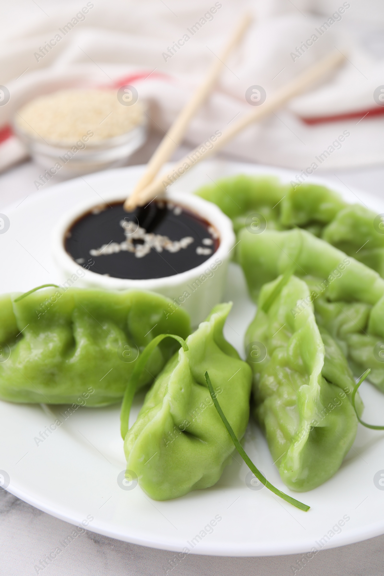 Photo of Delicious green dumplings (gyozas) and soy sauce on white marble table, closeup
