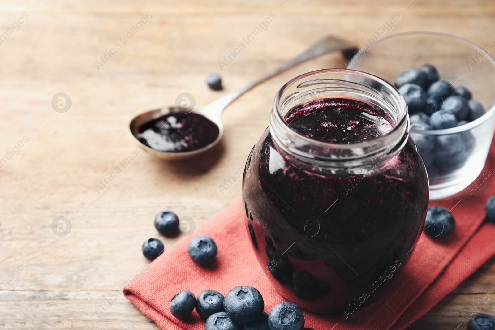 Photo of Jar of blueberry jam and fresh berries on wooden table. Space for text