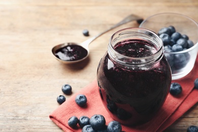 Jar of blueberry jam and fresh berries on wooden table. Space for text