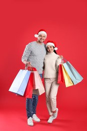 Photo of Happy couple with paper bags on red background. Christmas shopping