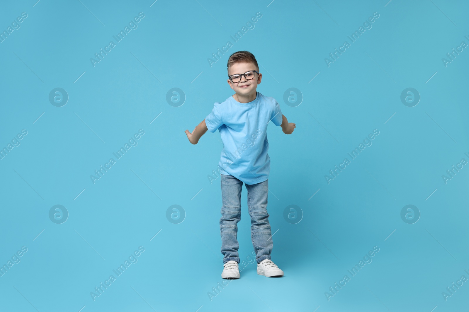 Photo of Happy little boy dancing on light blue background