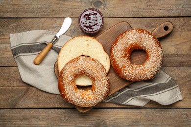 Photo of Delicious fresh bagels with sesame seeds and jam on wooden table, flat lay