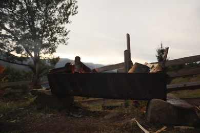 Photo of Old metal barbecue with burning firewood outdoors
