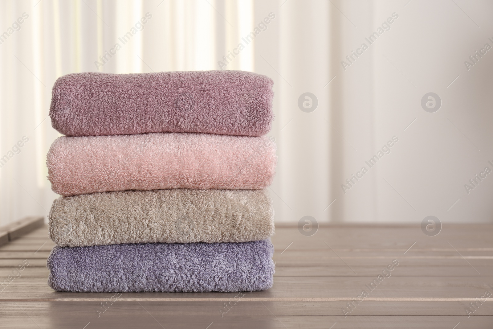 Photo of Stack of fresh towels on wooden table in bathroom. Space for text