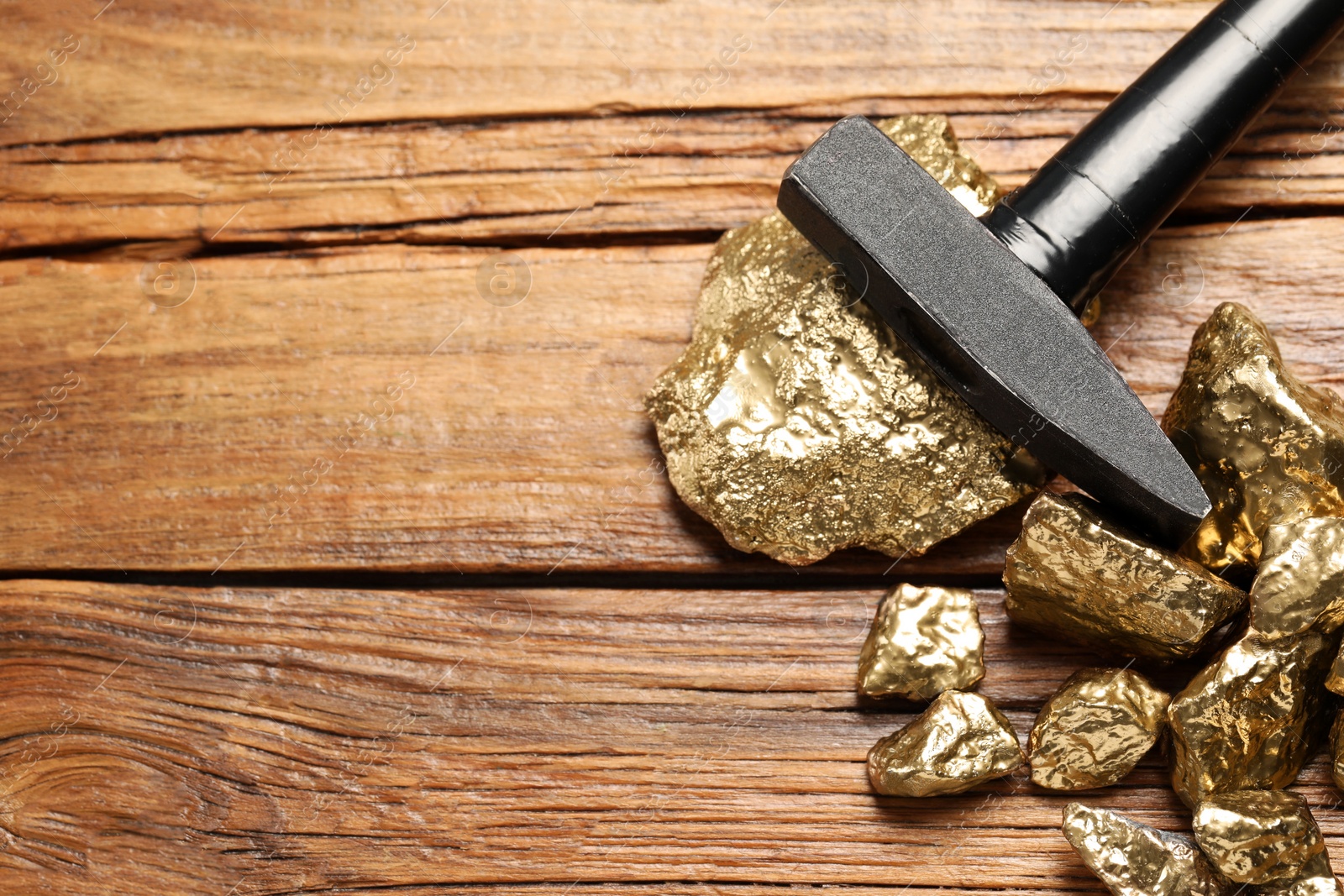 Photo of Pile of gold nuggets and hammer on wooden table, flat lay. Space for text