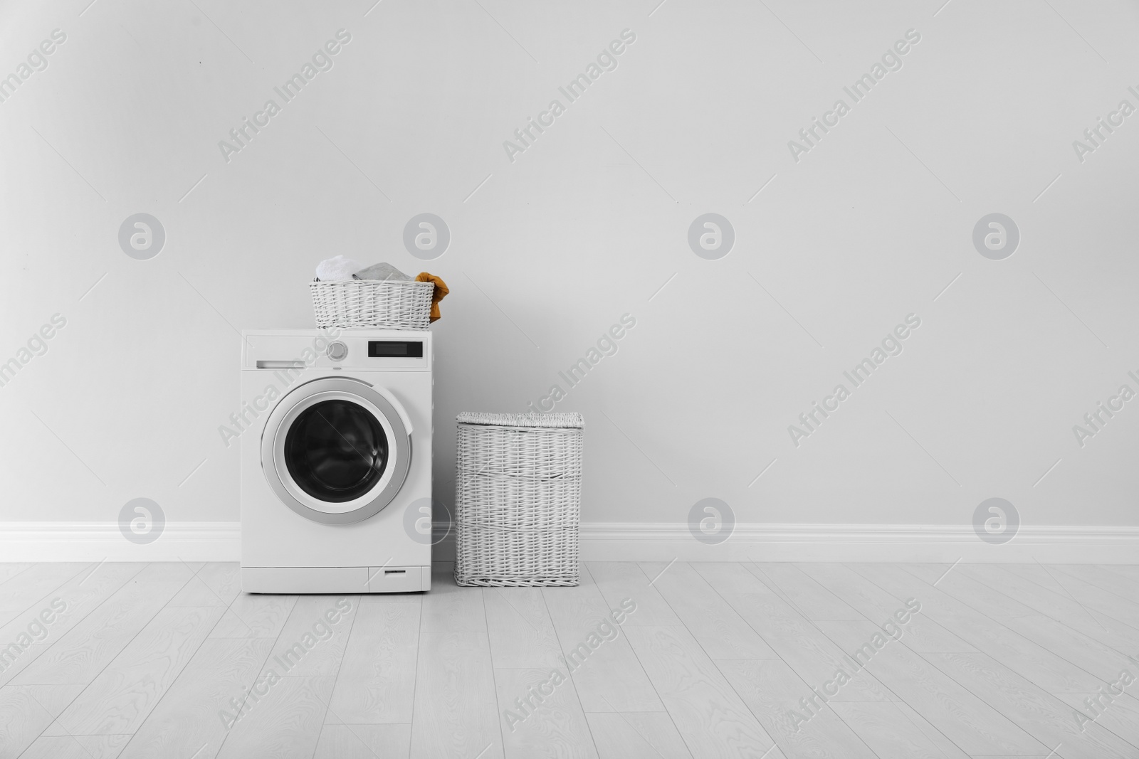 Photo of Washing machine with laundry and basket near wall. Space for text