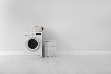 Photo of Washing machine with laundry and basket near wall. Space for text