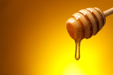 Photo of Pouring honey from dipper against golden background, space for text