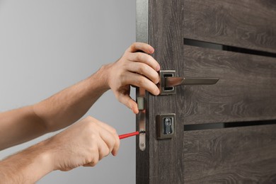 Worker with screwdriver repairing door lock indoors, closeup