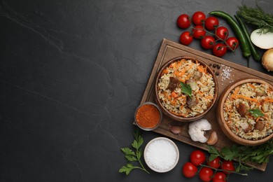 Photo of Delicious pilaf in bowls and products on black table, flat lay. Space for text