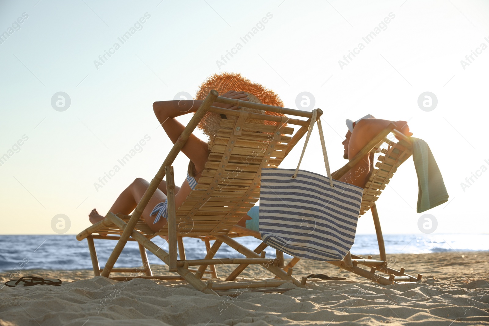 Photo of Young couple relaxing in deck chairs on beach near sea