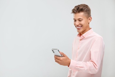 Photo of Happy young man sending message via smartphone on light grey background. Space for text
