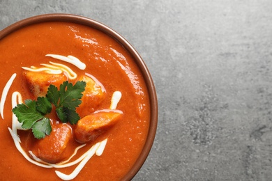 Photo of Bowl of delicious butter chicken on grey background, top view with space for text. Traditional indian Murgh Makhani