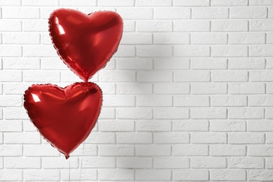 Photo of Red heart shaped balloons near white brick wall, space for text. Valentine's Day celebration