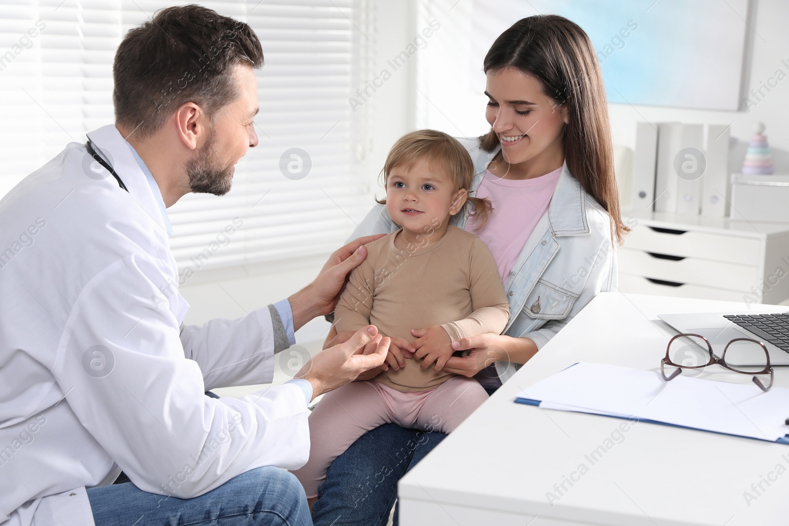 Photo of Mother and her cute baby having appointment with pediatrician in clinic. Doctor examining little girl